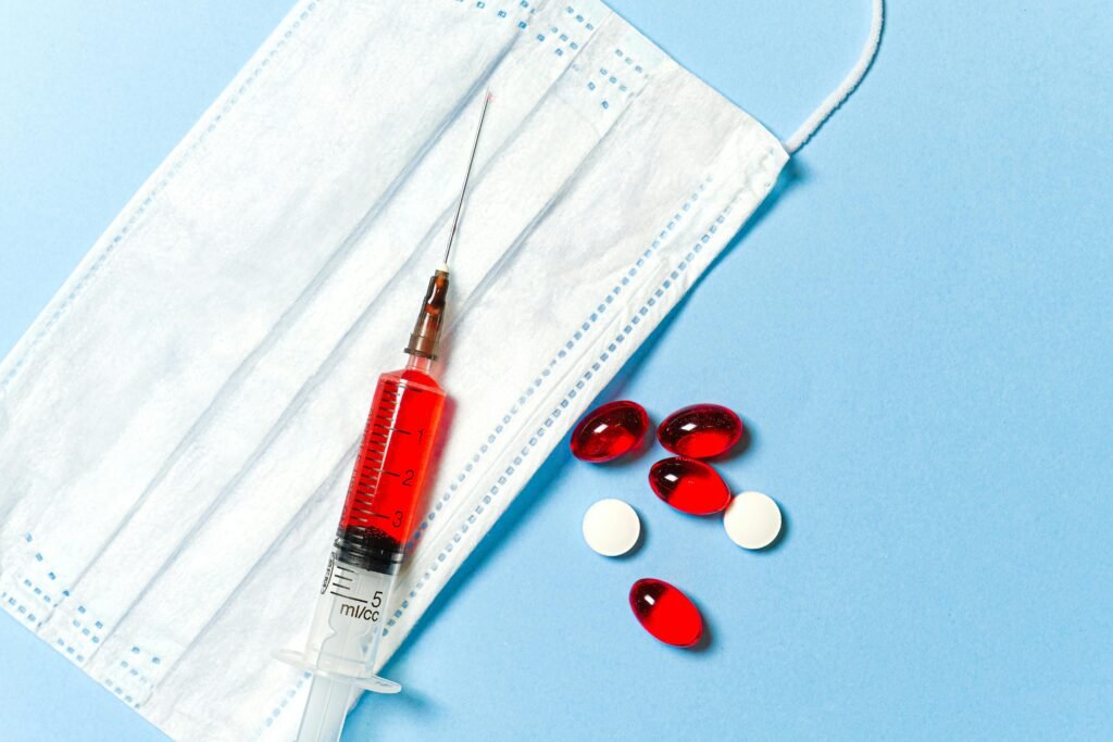 A syringe, face mask, and pills on a blue surface, symbolizing medical treatment. Weight loss.