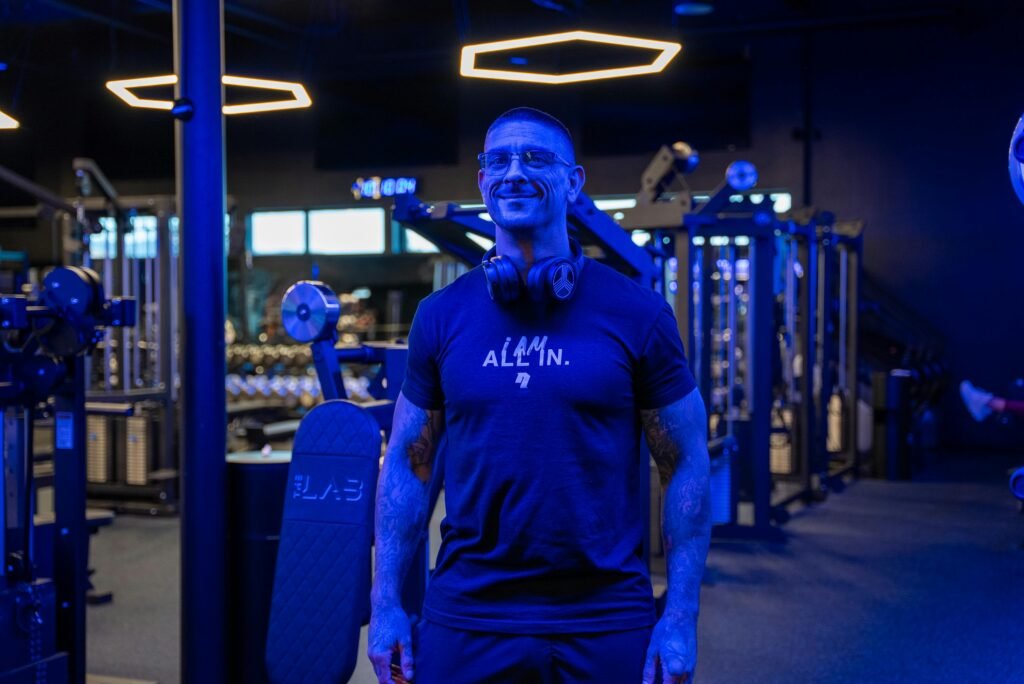 Athletic man with headphones smiling in a modern gym with blue lighting.